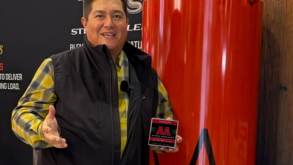 Man holding a box of Winchester AA Super Spreader ammunition speaking at a trade show.