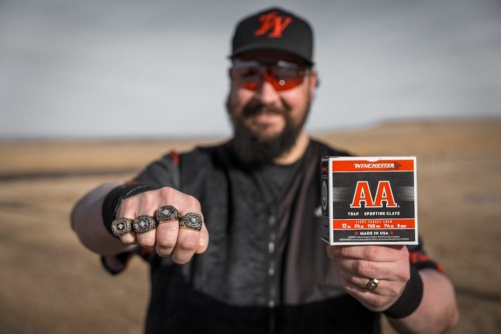 Professional Winchester shooter showing championship rings and a box of AA shotshells.