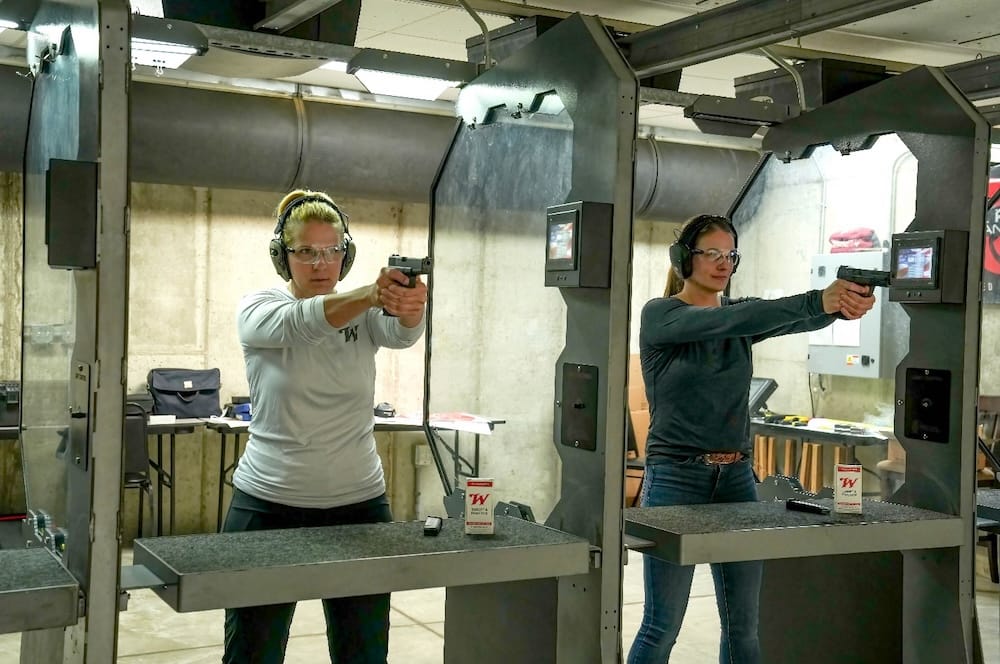 Two women at an indoor shooting range aiming down range.